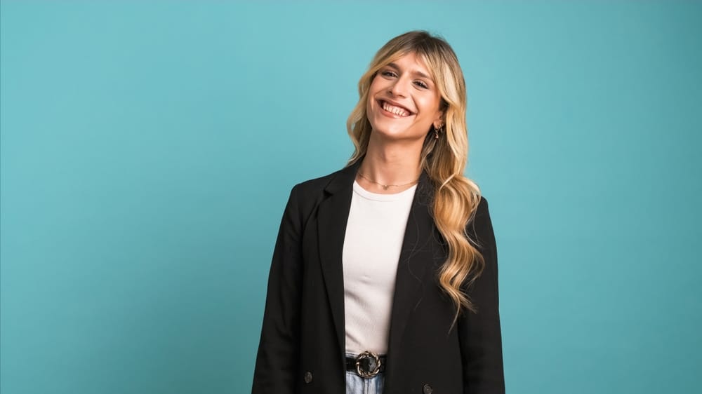 Cheerful transgender businesswoman laughing and looking at the camera against a blue background, representing confidence and results of laser hair removal.