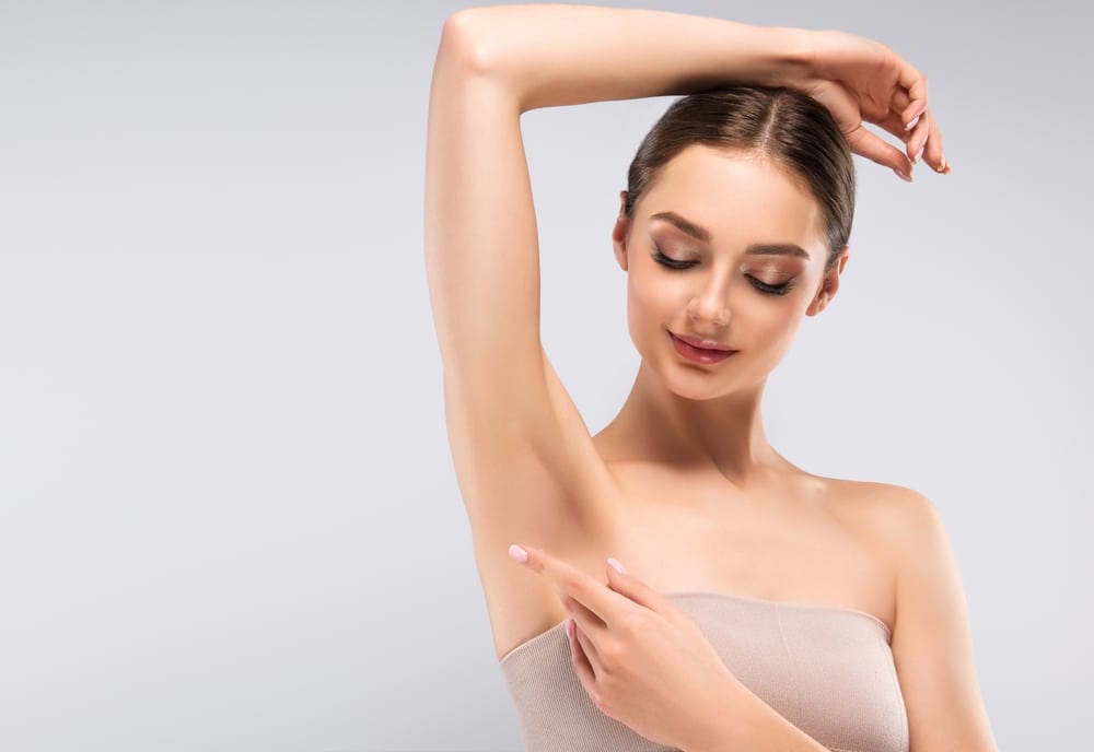 Young woman raising her arms to showcase smooth, hair free underarms after laser hair removal treatment, highlighting clear and radiant skin in a beauty and cosmetology context.