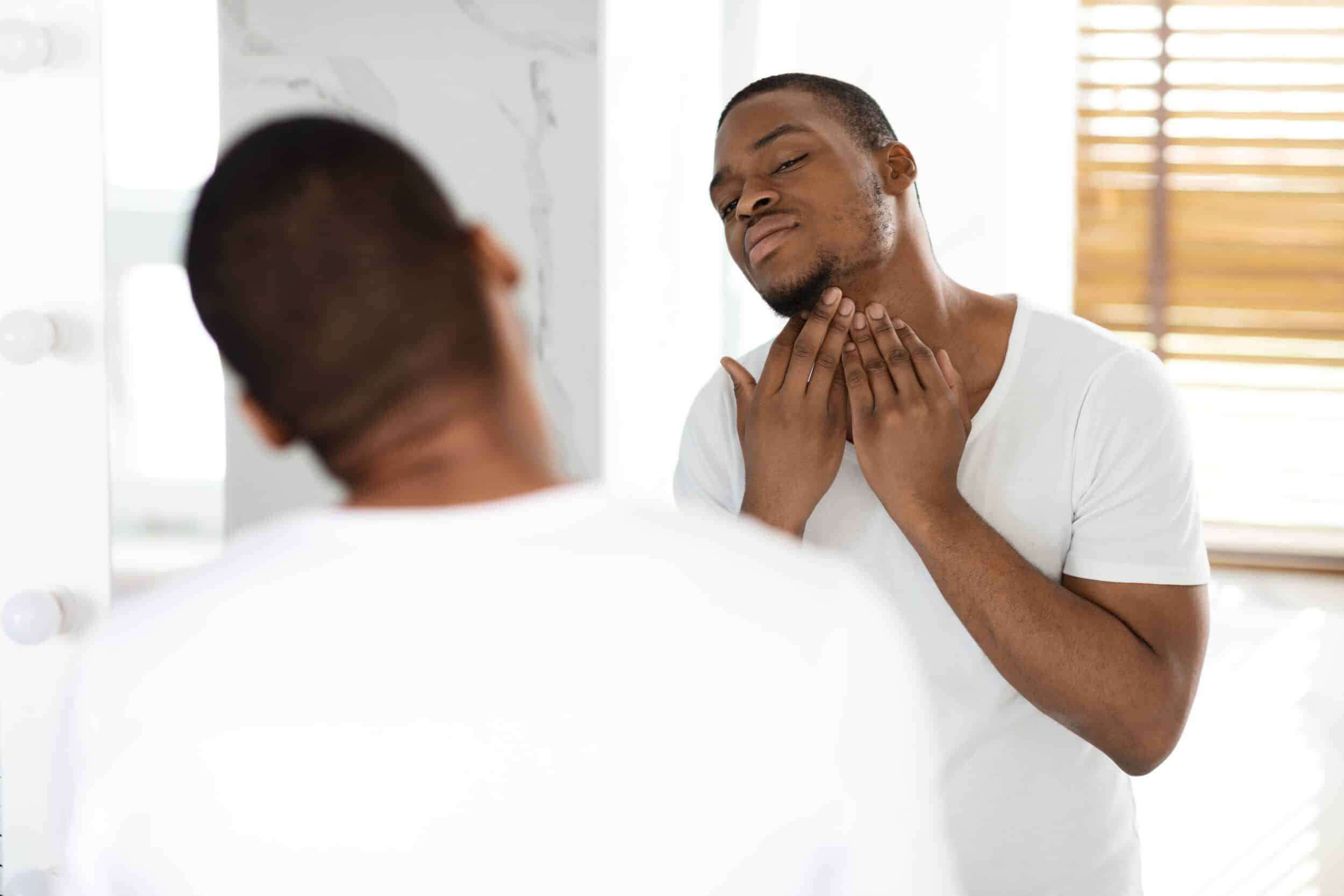 Man examining neck closely in mirror, showing discomfort from ingrown hairs and razor bumps, highlighting a common concern treatable with laser hair removal